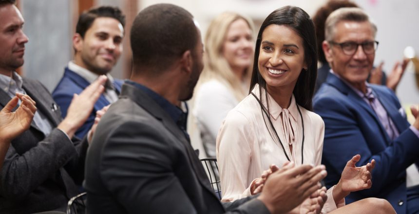 Group Of Businessmen And Businesswomen Applauding Presentation At Conference